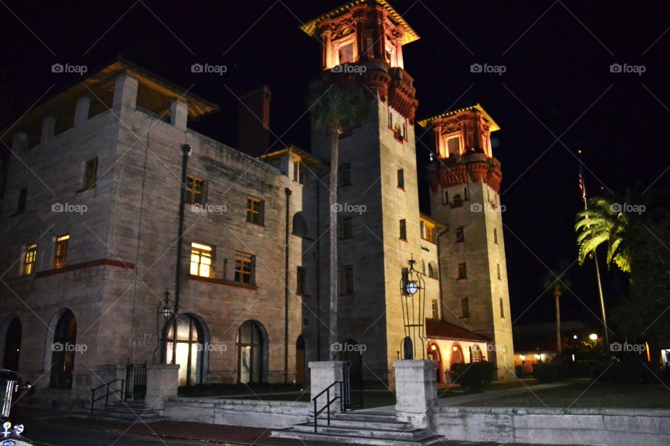 An old Spanish-styled building at night time with many windows and lights on and steps leading up to it