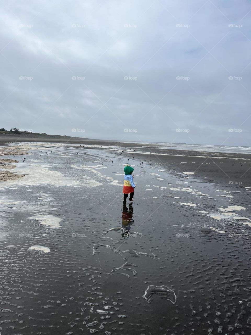 Child running on a beach in a bright raincoat
