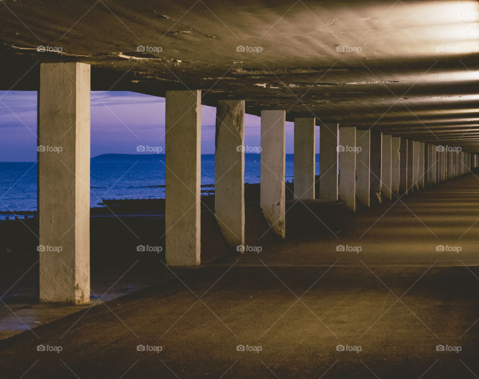 Pedestrian underpass known as Bottle Alley in Hastings, UK. The concrete columns create long shadows and the sea can be seen in the gaps between them.