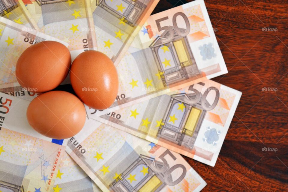 Euro money banknotes and three eggs on wood table.