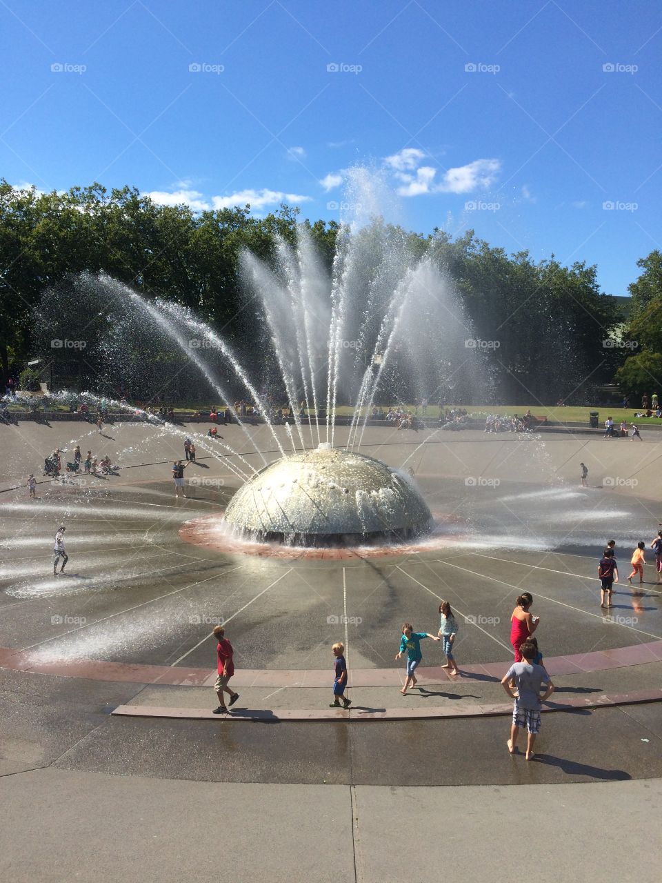 Kids and adults play in water fountain 