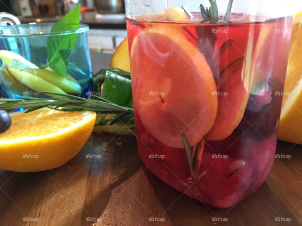 Flavored water with fresh raspberry lemon and orange with Rosemary herbs in kitchen making healthy refreshing summer hydration drinks 