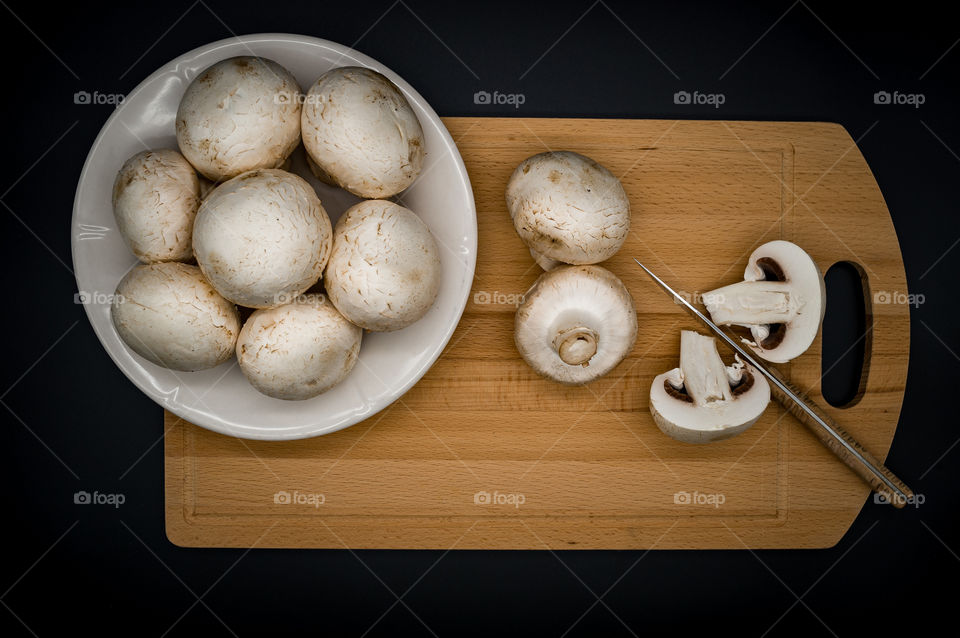 champignon mushrooms lie on a wooden cutting board next to a knife