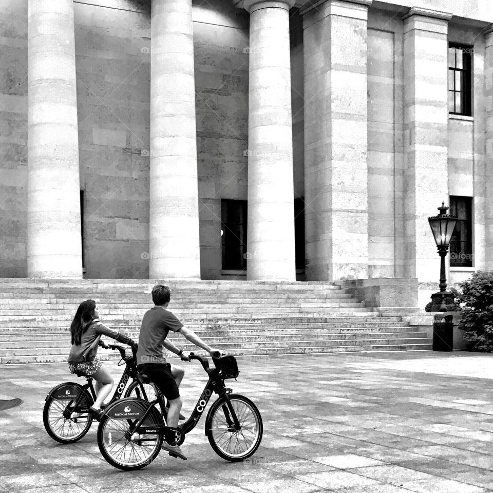 A couple ride bikes in a downtown city.