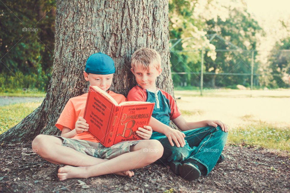 Two Young Boys by a Tree Reading a Book