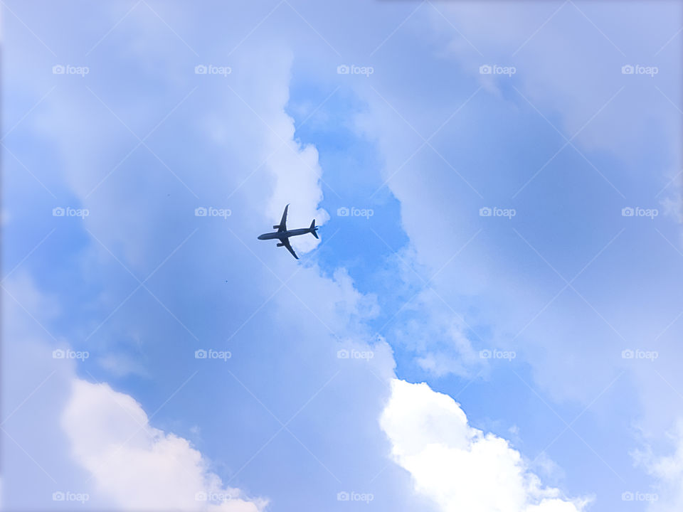 A commercial airplane flying above on a partly cloudy day at sundown. The sun is partially illuminating some of the clouds against a blue sky creating a majestic sight with patterns and beautiful blue and white hues.