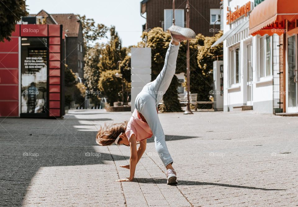 One little caucasian girl doing somersaults on a city street on a summer sunny day, close-up side view.