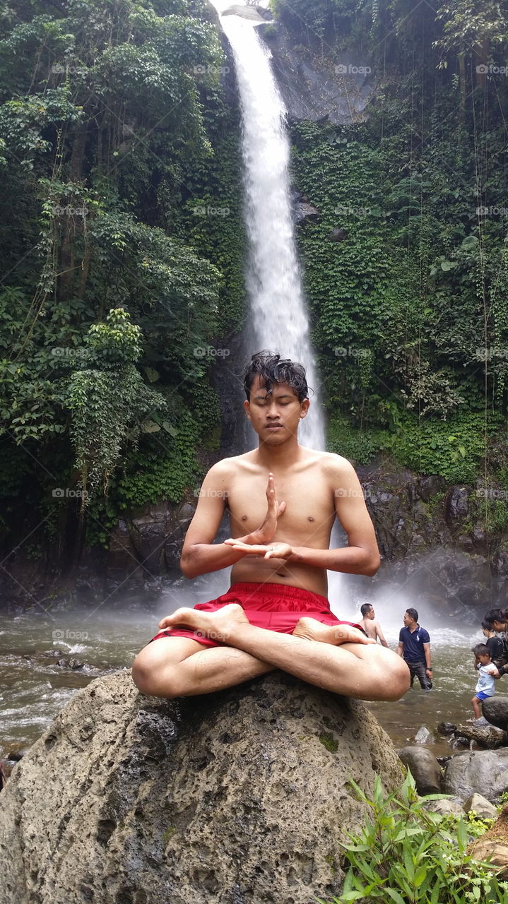 Teenage boy meditating under waterfall rocks