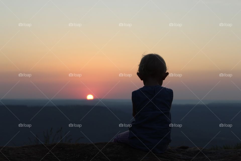 A child watches the sunset on a mountaintop alone 