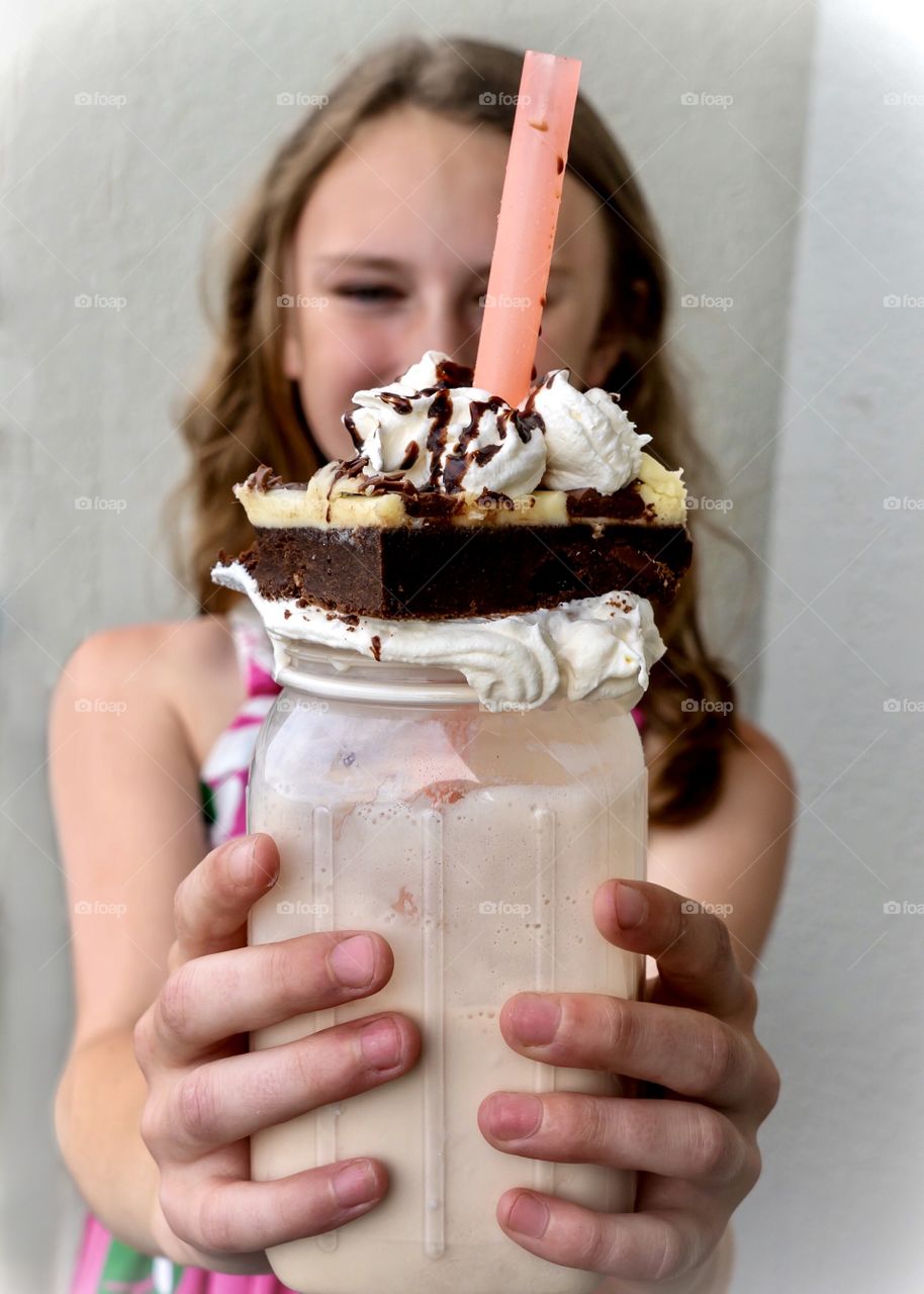 Girl holding a decadent milkshake drink in a jar topped with a chocolate brownie cake and whipped cream 