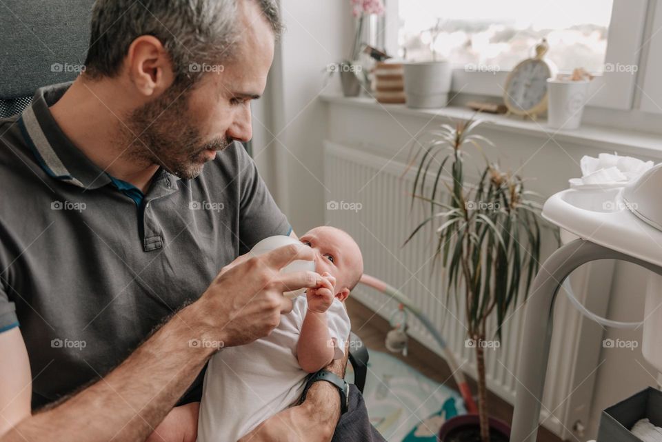 Father feeding his baby son with bottle of baby formula