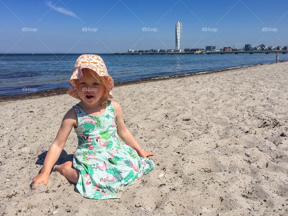 Little girl of three years old playing in the sand at Ribban bech in Malmö Sweden with the famous skyscraper Turni g Torso in the background.