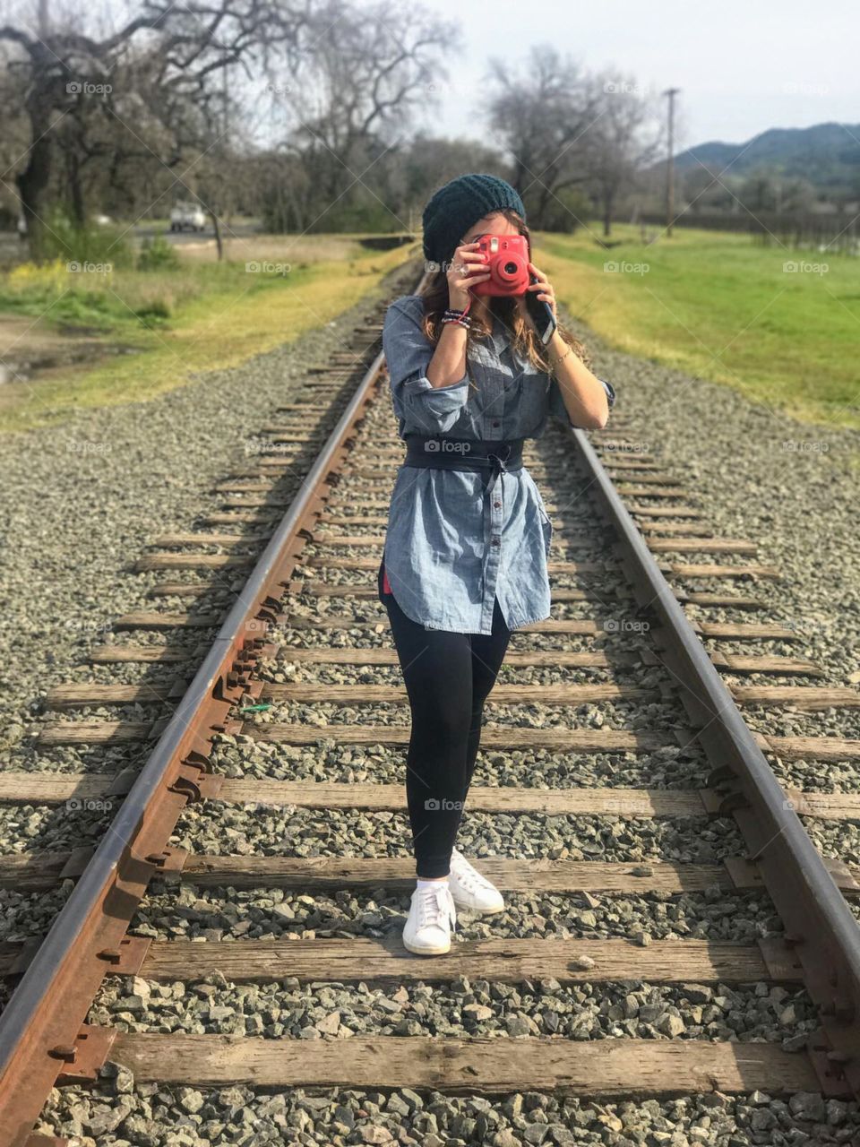 A woman taking a picture with her red polaroid.  she's on a train line in Napa Valley