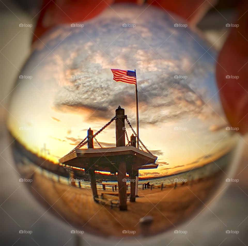 The American flag on a flag pole blowing during a sunset scene on a dock.