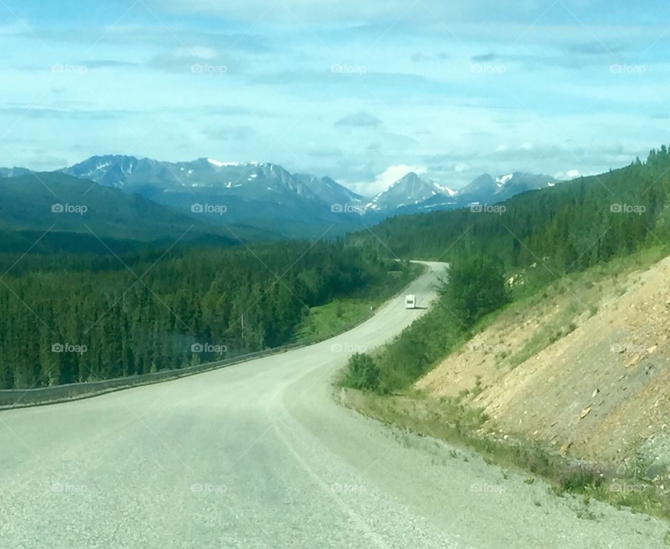 A Long and Winding Road. A lone camper RV travels the lonely Alcan Highway somewhere in Canada's Yukon Territory.  Driving through endless beauty