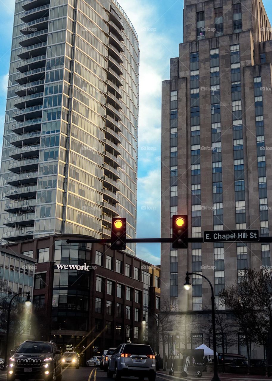 Cars driving around the city near tall buildings.