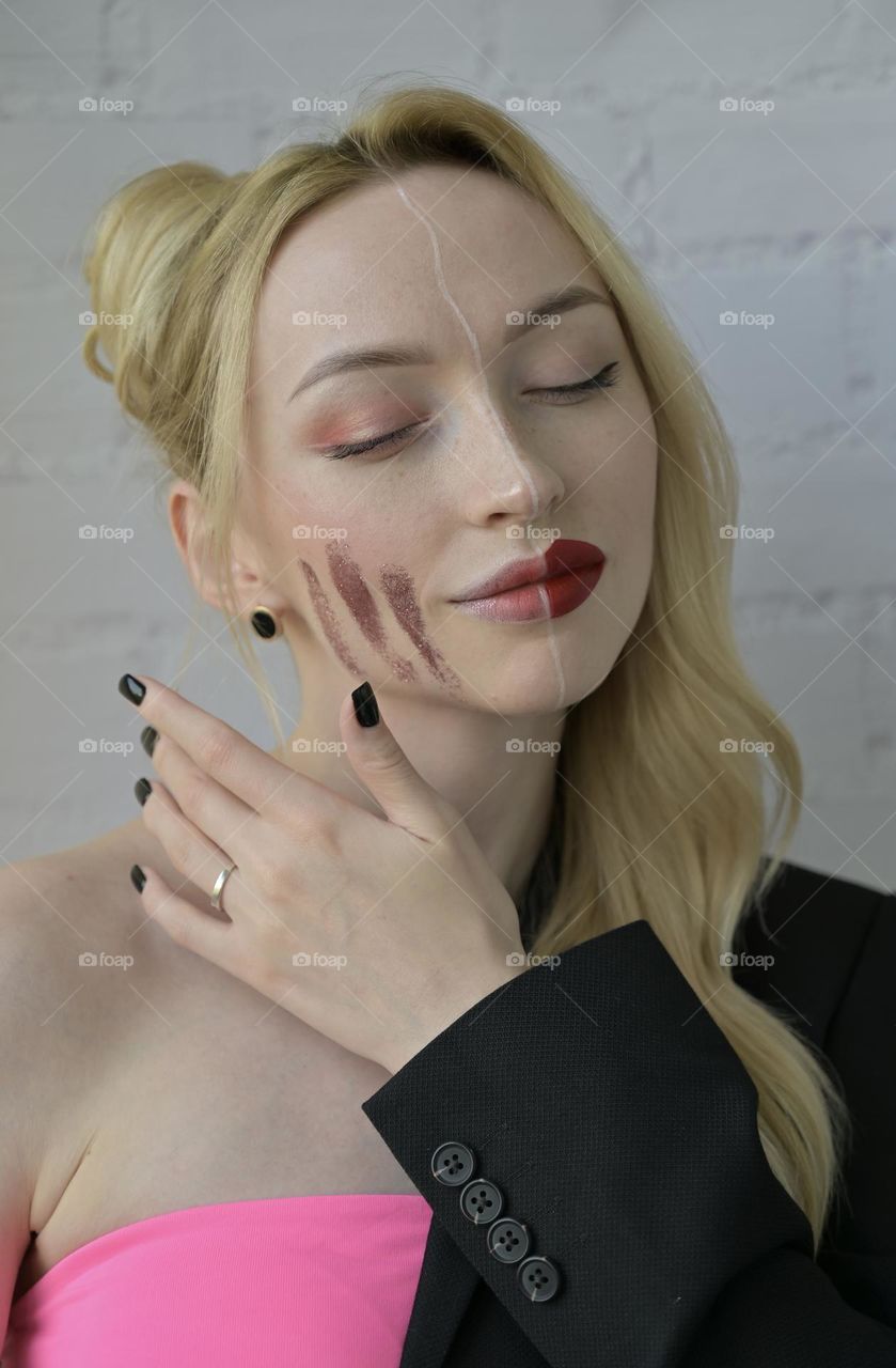 Close-up portrait of a blonde smiling girl with different make-up on half of her face with hand near face on white background