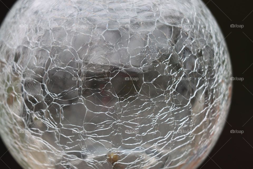 A glass sphere against a black green background, constraining with all its cracks.