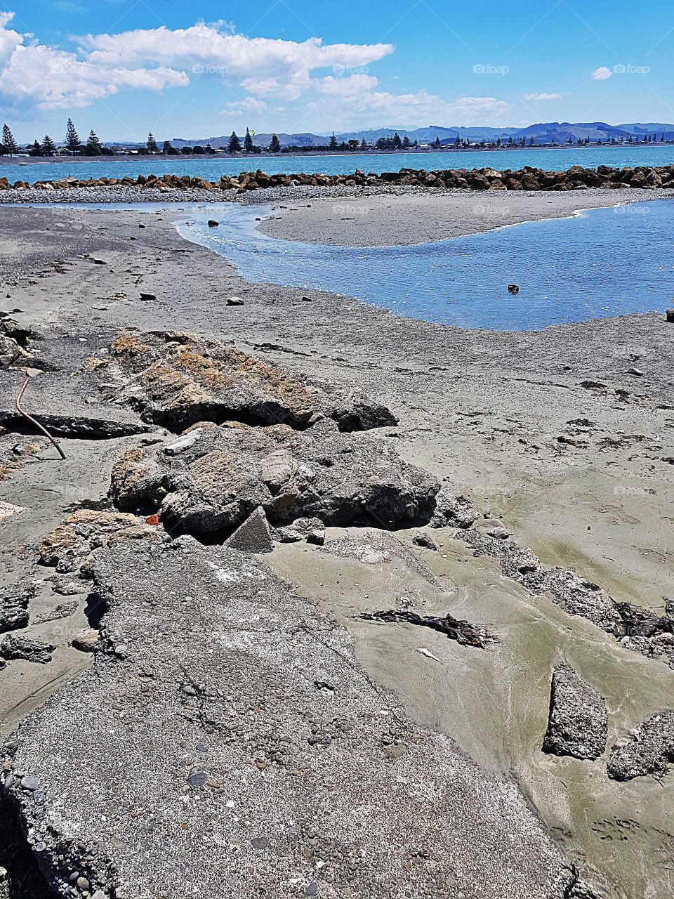As the tide goes out the scene left behind of rock pools small river like pools and beyond the rocks is part of the Hawkes Bay. beyond that is west shore and the ranges in the horizon.