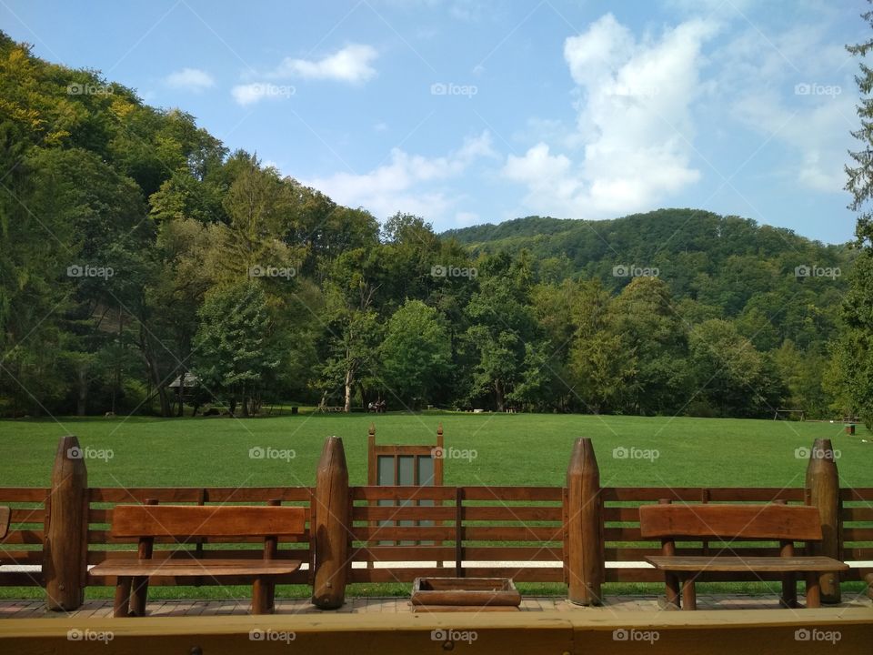 Peaceful train station in the mountains, warm tones of the fencing and benches compliments the vibrant green of the surrounding nature.
