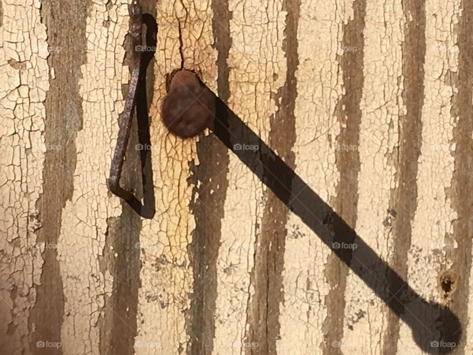 Peeling paint on weathered piece of wood, rusted nail and its shadow, textural interest 