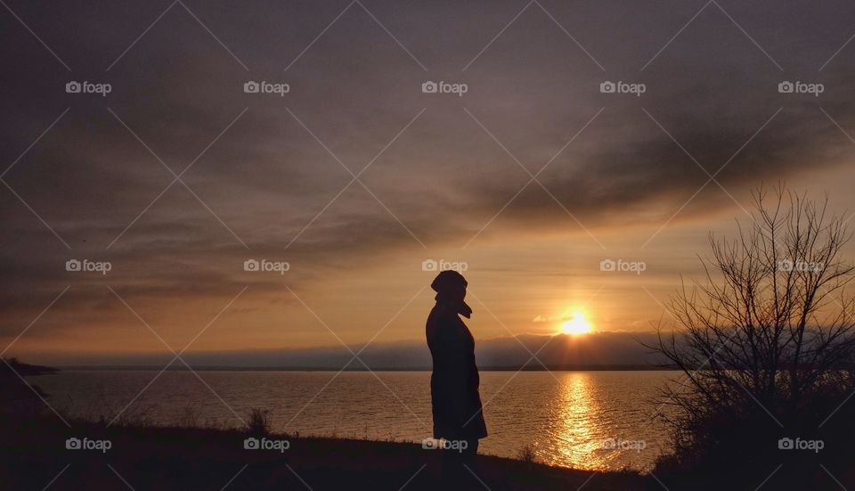 A lady stands by the river and look at a sunset. 