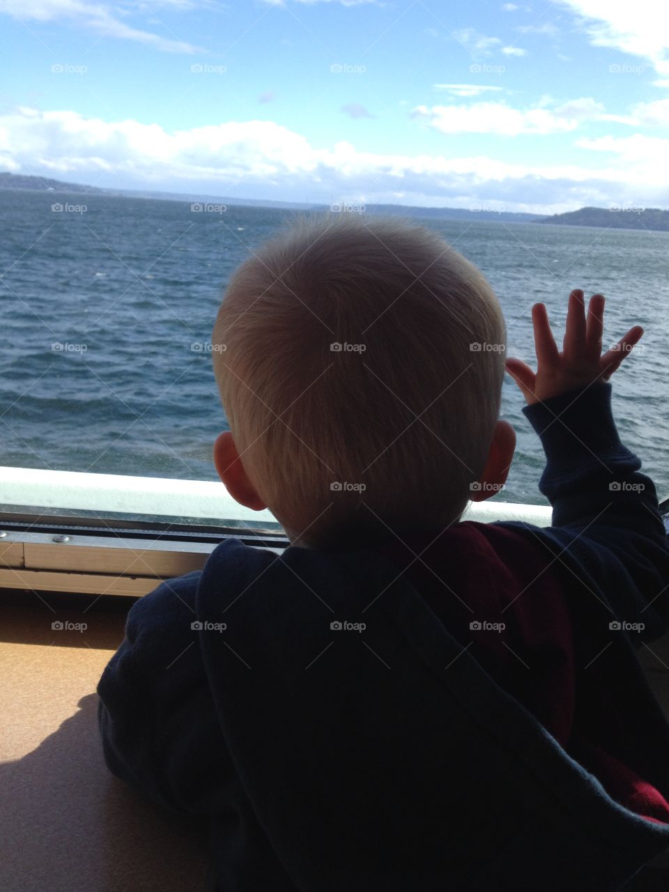 Ferry Ride. A toddler tries to touch the water through the ferry window.