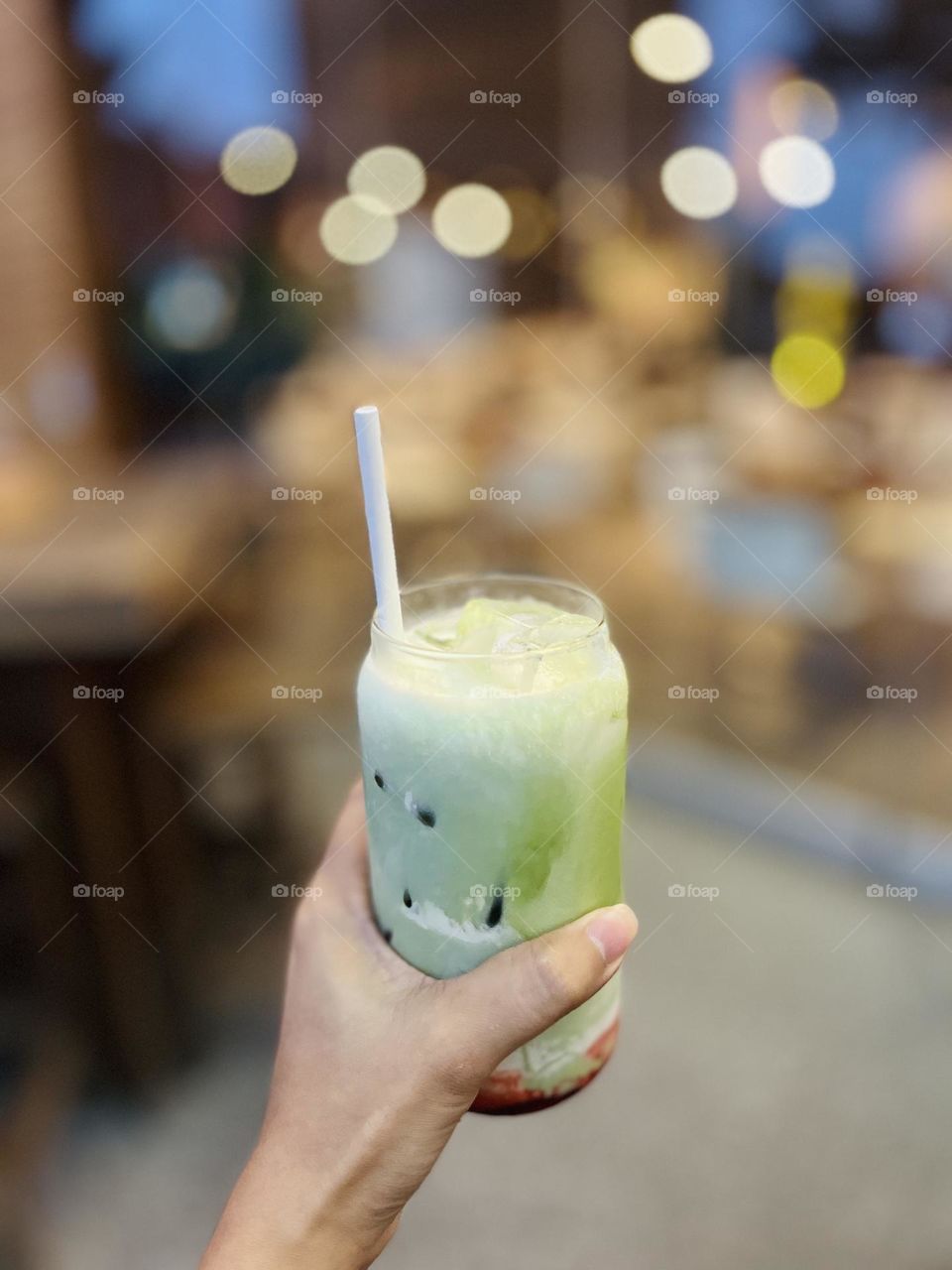 Hand holding a glass of cold drink in a restaurant in the evening