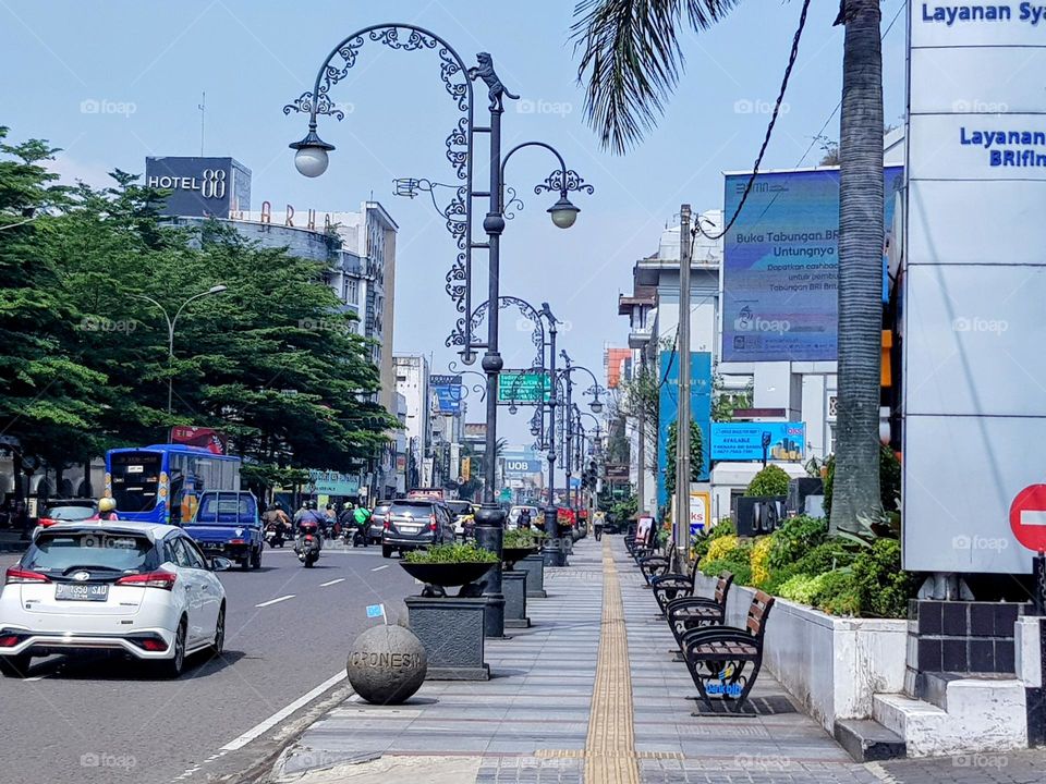 Decorative lights along Jalan asia africa, front of the bandung alun alun, poles made steel, curved design, white lights, at the top there is a lion, on the sidewalk filed with flower pot, round stone and long benches