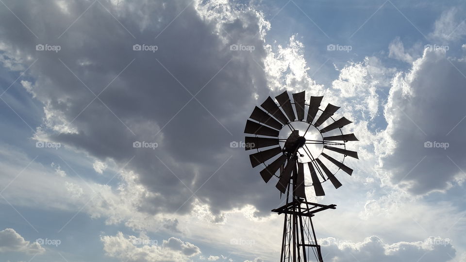 old grey metal windmill standing alone in a field with a dramatic sky as it's backdrop is a beautiful grey stormy story