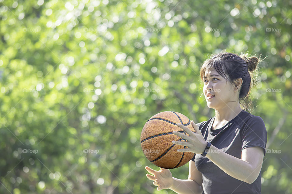 Basketball in hand Asian woman Background blur tree in park.