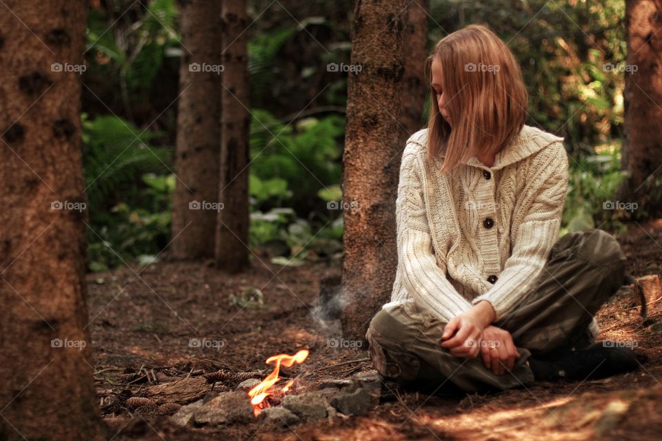 Girl sitting by the fire in a knitted boho sweater in the mountains