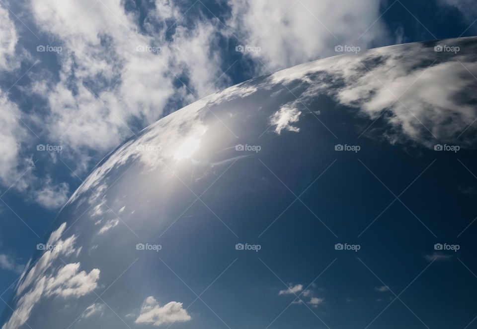 Blue sky with fluffy white clouds reflected on a curved mirror structure 