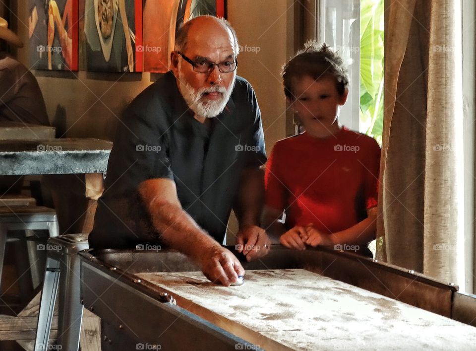 Grandfather And Grandson. Grandfather Playing Shuffleboard With Young Grandson
