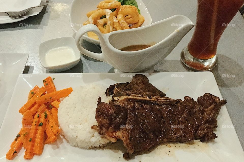 Steak with rice, buttered carrots and onion rings as a side dish.
