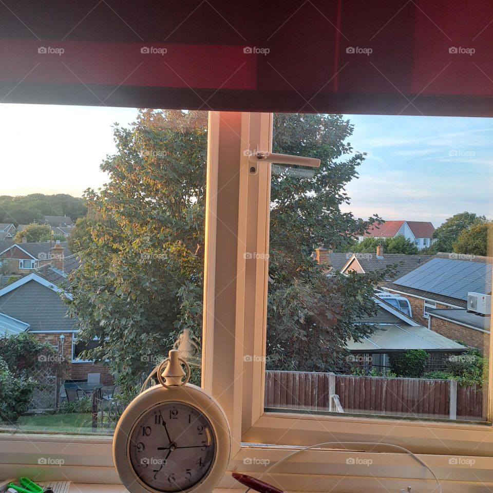 uk window view early eve. late summer. soft light. windowsill, clock, tree outside. rooves