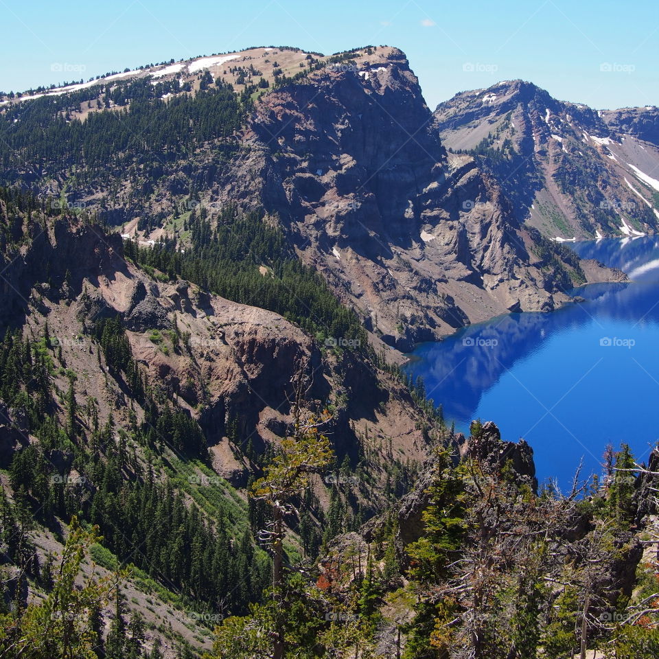 The jagged rim reflecting into the rich blue waters of Crater Lake in Southern Oregon on a beautiful summer morning with perfect clear blue skies. 