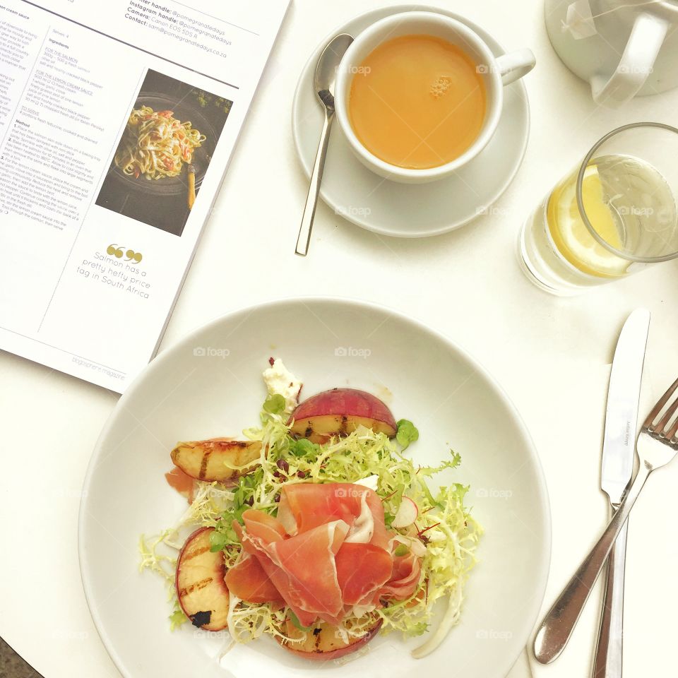 White table with salad of peaches and Parma ham with a cup of tea. 