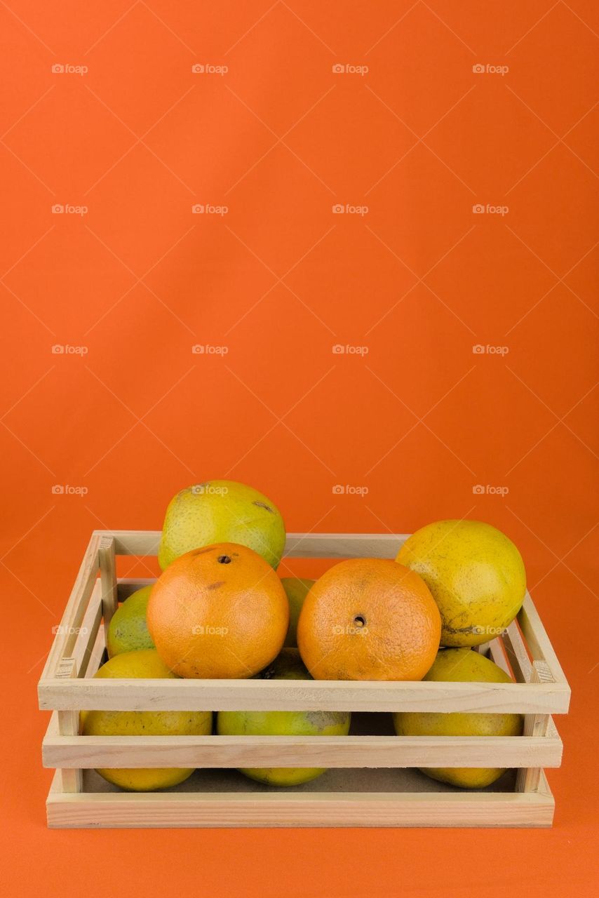 Wooden box with tropical oranges on orange colored background