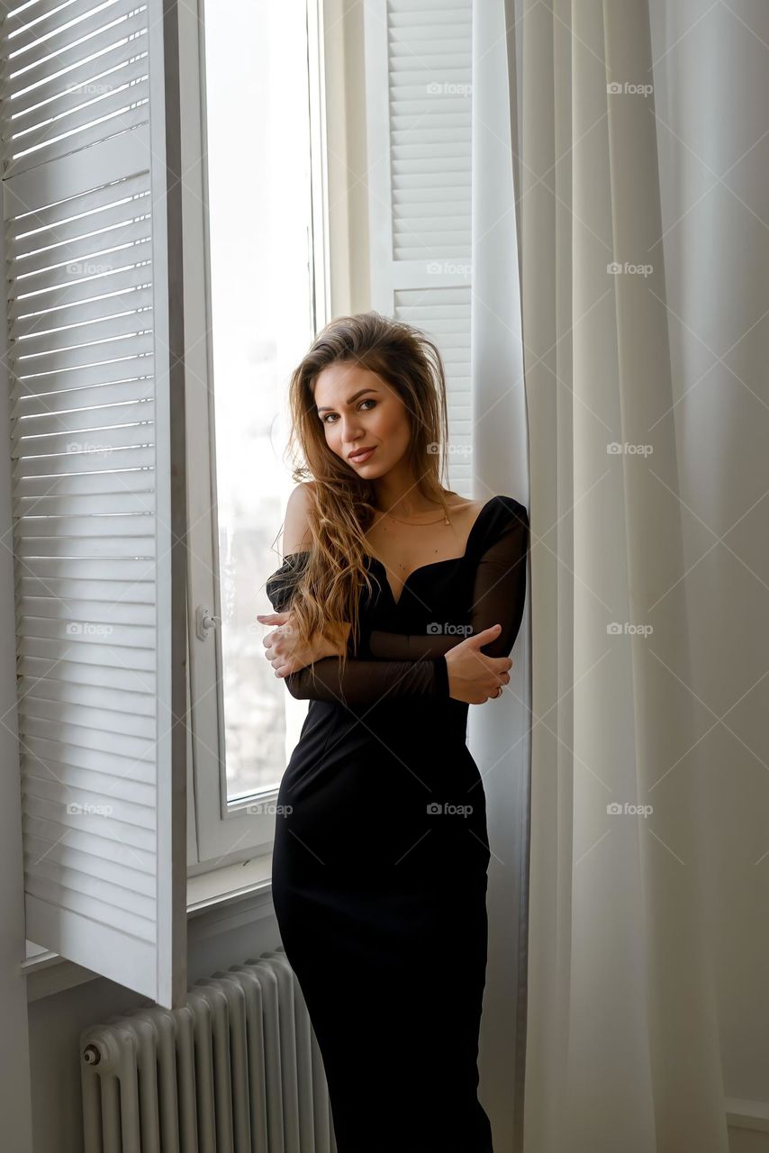 Beautiful woman in black dress near window 