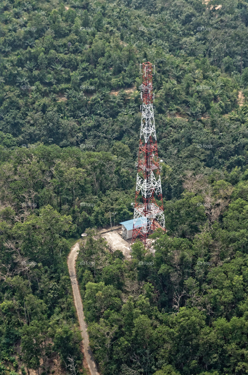 Rural telecommunications tower at the top of a hill surrounded by forest with its access road and power generator