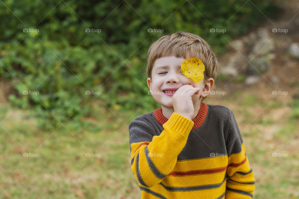 Portrait of a smiling boy holding a yellow leaf near his face in forest in autumn male child picnic outdoors weekend