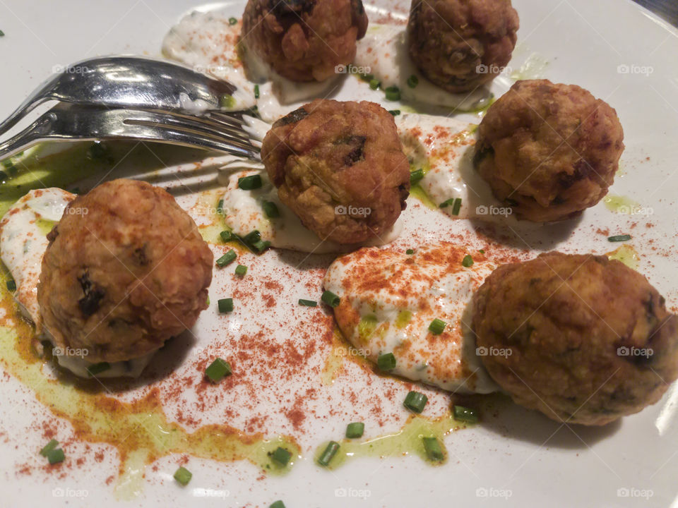 Fried meatballs with yoghurt sauce served on a plate.