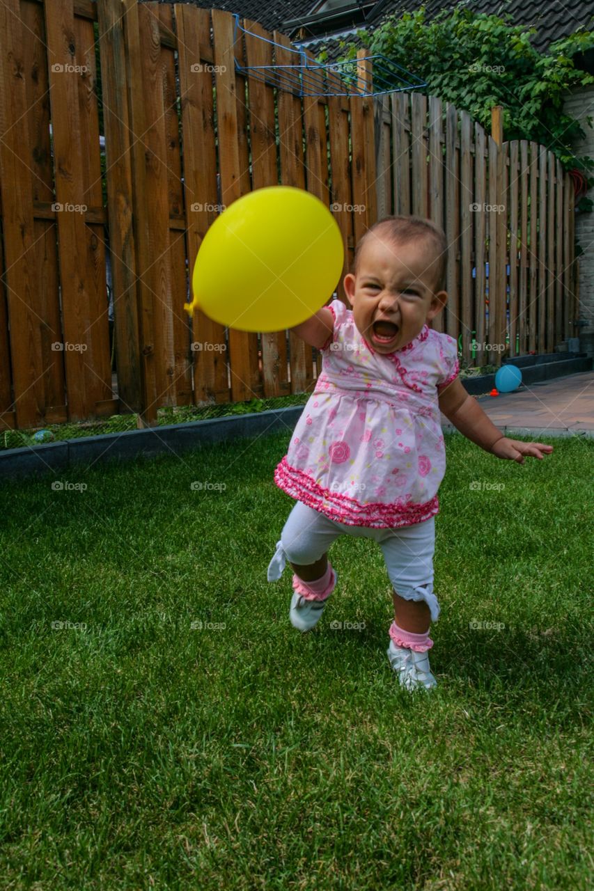 Little girl walking and screaming with her balloon on the grass. Her first birthday and she just loves the balloon