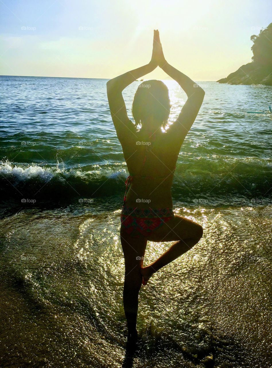 Child in yoga pose on beach at sunset