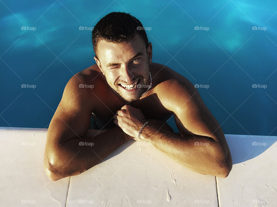 Young smiling man in the blue swimming pool 