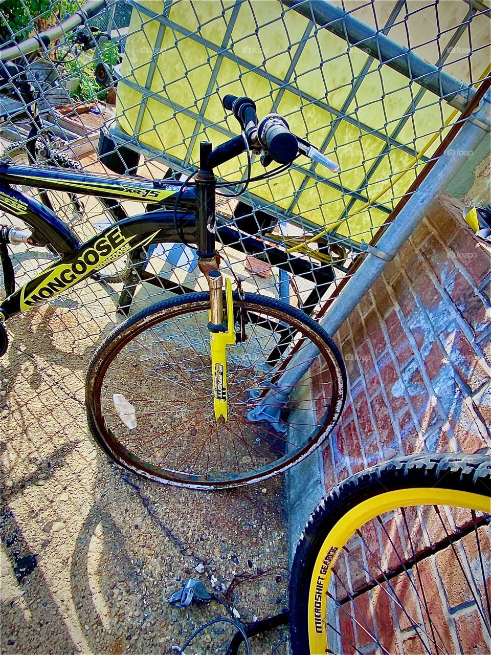 Bicycles as well as bicycle parts are being stored aside an old building off „Borden Ave“ by the „Pulaski Bridge“ at „Newtown Creek“ leaning up against the exposed brick wall and a yellow plastic pane. 2022. Hypnotic Productions