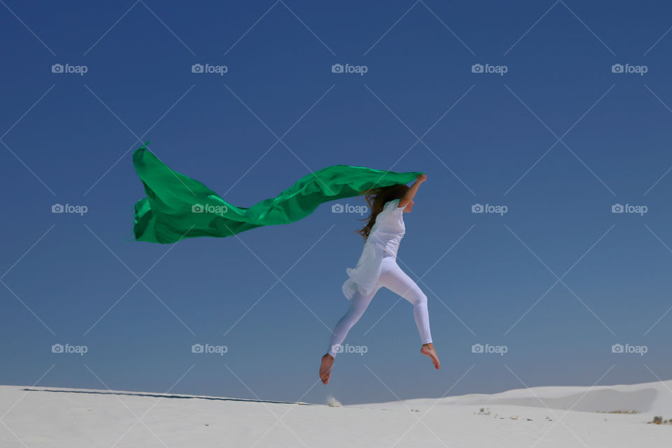 Woman jumping on sand with holding green fabric