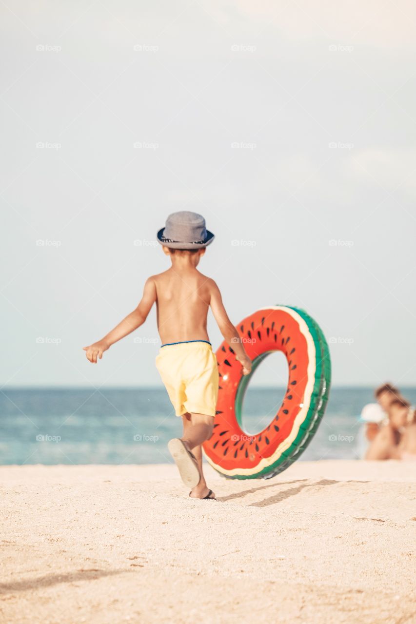 A little boy with watermelon swimming circle at the beach