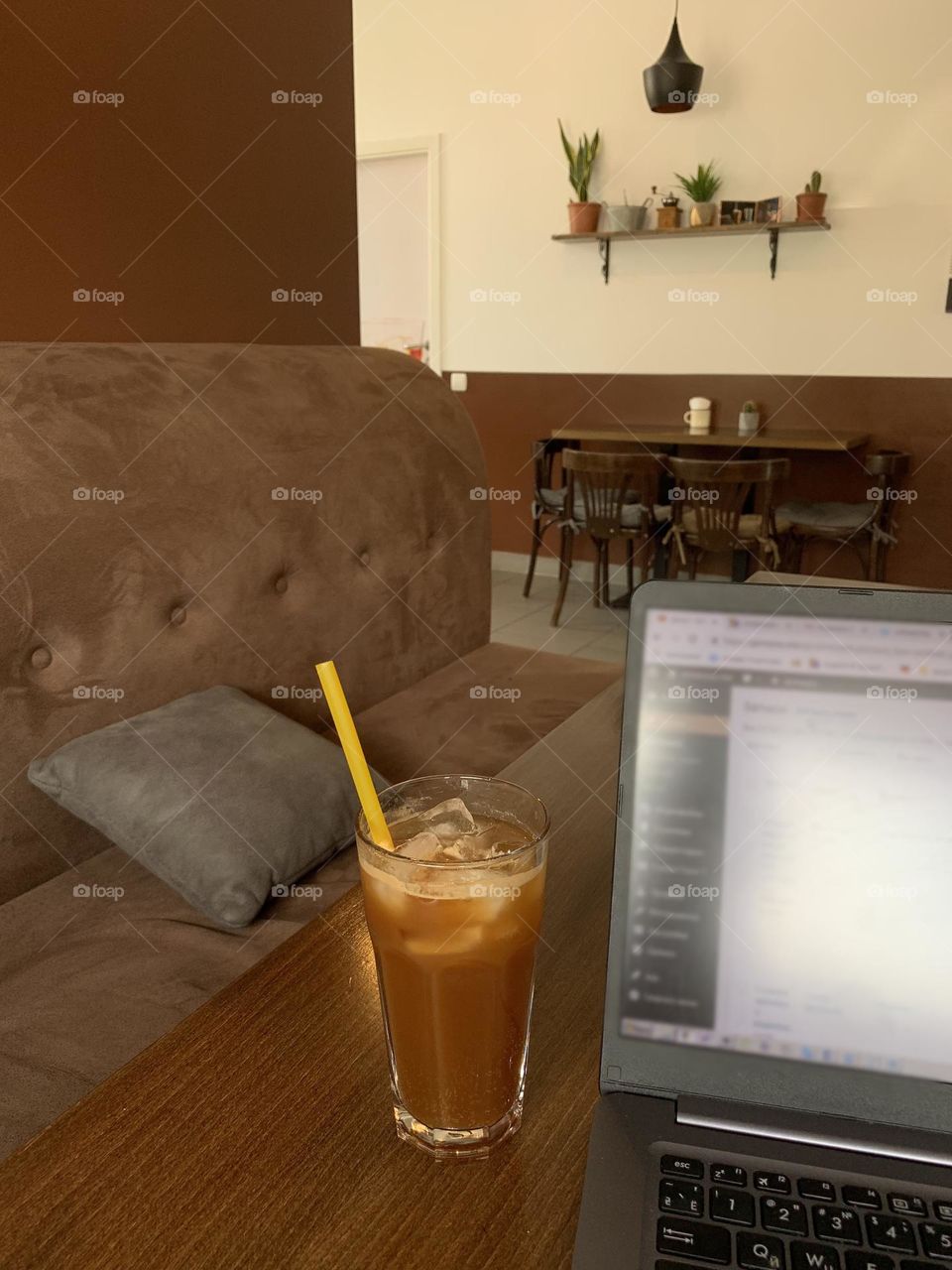 Working in the cafe with my laptop, enjoying coffee and the atmosphere. Coffee glass with a straw, laptop on the table, empty cafe with no people around